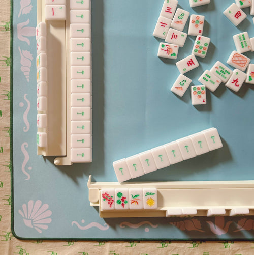 White Mahjong tiles from island collection on a blue Mahjong mat with light pink seashell and ocean-inspired border. Each tile size: 1" x 1 7/16" x 7/16". 